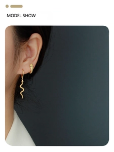 Detail of gold snake-shaped hoop earring and pendant worn by model on a dark background