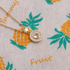 Detailed view of a gold heart pendant necklace with shimmering zircon stones on fabric