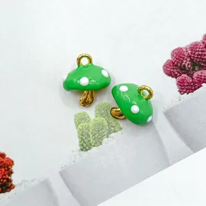 Macro shot of green enamel mushroom charms with white polka dots and gold loop metal hooks