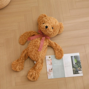 Brown curly plush teddy bear with red gingham bow sitting on light wood flooring
