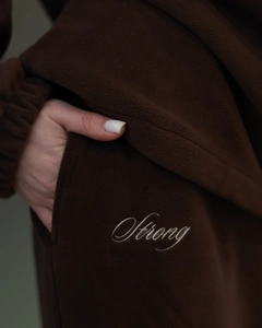 Detail of dark brown polar fleece jacket featuring white 'Strong' letter embroidery and side pocket