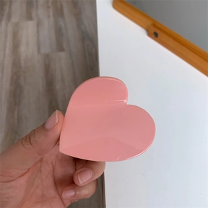 Detail view of pink heart-shaped acetate hair claw clip held in hand for size display