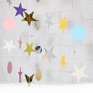 Hanging Christmas paper garland featuring colorful star and circle shapes on a white wall