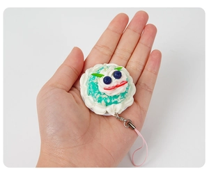 Miniature fake cake charm featuring blueberries and strawberries held by hand