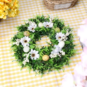 Easter wreath with white daisies, green leaves and painted eggs on a checkered tablecloth