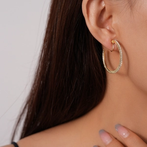 Close-up of a gold clip-on hoop earring with clear rhinestones on a female ear