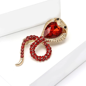 Golden snake brooch with red rhinestones and crystal teardrop on a white display