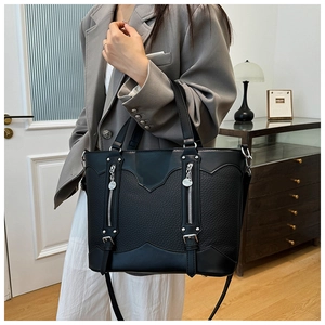 Detail of black patchwork leather tote with zippers shown on a model in a modern room