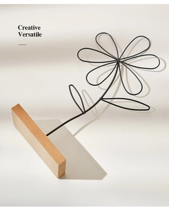 Close-up of minimalist black iron wire flower sculpture with a solid wood base