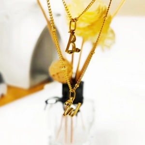 Détail des pendentifs lettres B et W dorés à l'or fin sur chaînes à billes fines