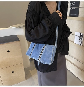 Blaue Denim Umhängetasche mit Reißverschluss-Details, am Model in Innenräumen präsentiert
