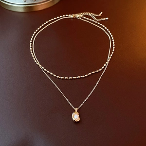 Close-up of a double-layered gold necklace with beads and a pearl pendant on leather