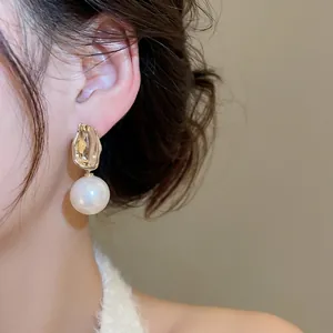 Elegant gold textured metal earrings with large round pearls worn by a model in a close-up view