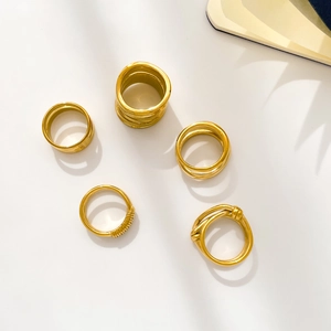 Flat lay of multiple 18K gold-plated knotted and layered rings with soft shadow