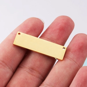 Gold rectangular stainless steel pendant with double holes shown on a finger for size scale