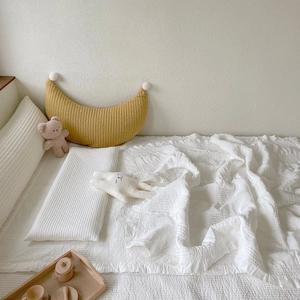 Detail of yellow moon nursing pillow and white quilted cotton bedding for baby nursery