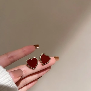 Detailed close-up of red heart earrings with golden metal edges held in hand