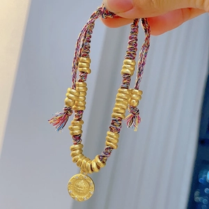 Close-up of ethnic beaded bracelet with golden ring spacers and round engraved pendant charm