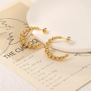 Elegant gold beaded C-shape hoop earrings arranged on a white tray with vintage props