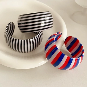 Macro shot of wide striped resin bangles with glossy finish on a white ceramic tray