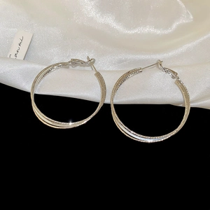 Detailed macro shot of 18k silver double layer cross hoop earrings on white silk fabric