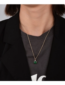 Close-up of gold chain necklace with a green round gemstone and white zircon on a model