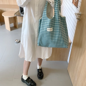 Detail view of the blue checkered knit tote bag carried by a model in a minimal setting