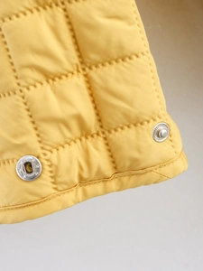Macro view of bright yellow quilted fabric with silver snap buttons and stitched detailing