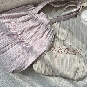 Detail of Bonjour embroidery and pleated striped fabric on two large canvas tote bags