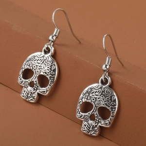 Vintage silver skull earrings with intricate floral carvings on a brown pedestal
