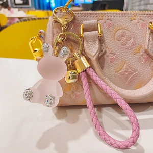 Pink resin bunny keychain with rhinestones shown as a decorative charm on a designer handbag