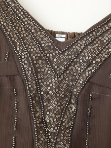 Detailed close-up of V-neckline featuring intricate silver sequins and beadwork on brown fabric