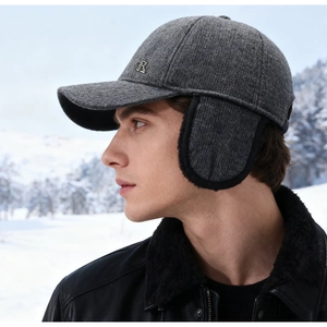 Détail d'une casquette d'hiver grise avec protège-oreilles et logo R en métal sur neige