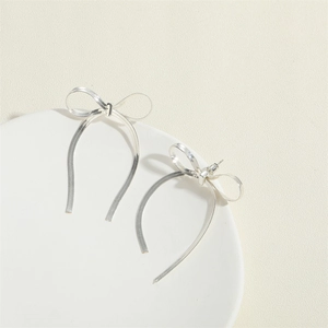 Detail of silver bow tassel earrings featuring long snake chain fringes on a stone tray