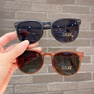 Foldable UV400 children's sunglasses in black and tawny frames shown against a brick wall