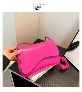 Detail of rose red flap crossbody bag with knot shoulder strap and curved edge