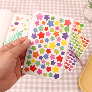 Colorful star stickers held over a pink plaid tablecloth for DIY journals and crafts