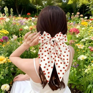 Detail of strawberry print hair bow clip worn on a model in a garden setting