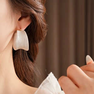 Macro shot of white irregular shell texture hoop earring with gold posts on a model