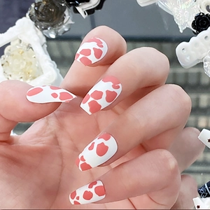 Close-up of matte red and white cow pattern press-on nails in long coffin shape