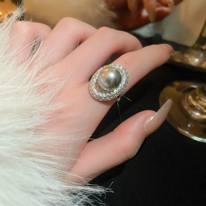 Detailed view of an oval dark grey pearl ring with double halo crystals on a hand