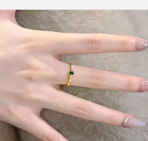 Macro detail of golden bamboo-shaped ring with a centered emerald green bead inlay
