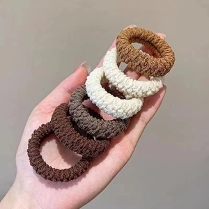 Close-up of five thick knitted elastic hair ties in autumn earth tones held in hand