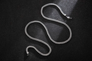Close-up of a silver stainless steel curb chain necklace with a lobster clasp on dark background