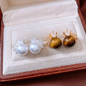 Detail of 18K gold plated tiger eye earrings and pearl studs in a beige jewelry box