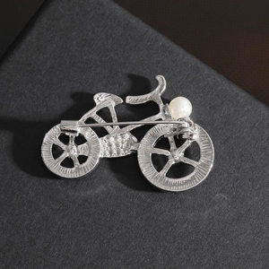 Broche vélo argentée avec perle dotée d'un fermoir de sécurité rotatif au dos