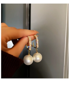 Gros plan de boucles d'oreilles en U dorées serties de zircons avec grosse perle blanche
