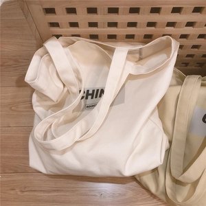 Détail de grands sacs fourre-tout en toile épaisse blanche et beige avec lettres noires