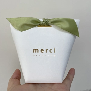 Close-up of white textured gift box with green satin bow and gold merci lettering