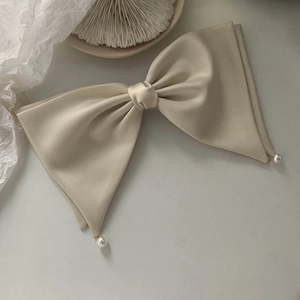 Detailed macro view of cream satin bow hair clip with elegant hanging pearl charms
